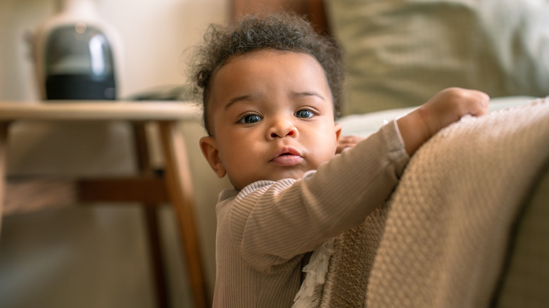 A baby holding a blanket staring directly at the camera