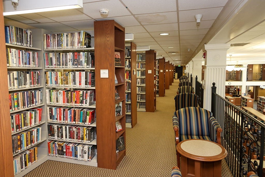 Library interior with numerous bookshelves filled with a variety of books. A seating area with striped chairs and a table is in the foreground
