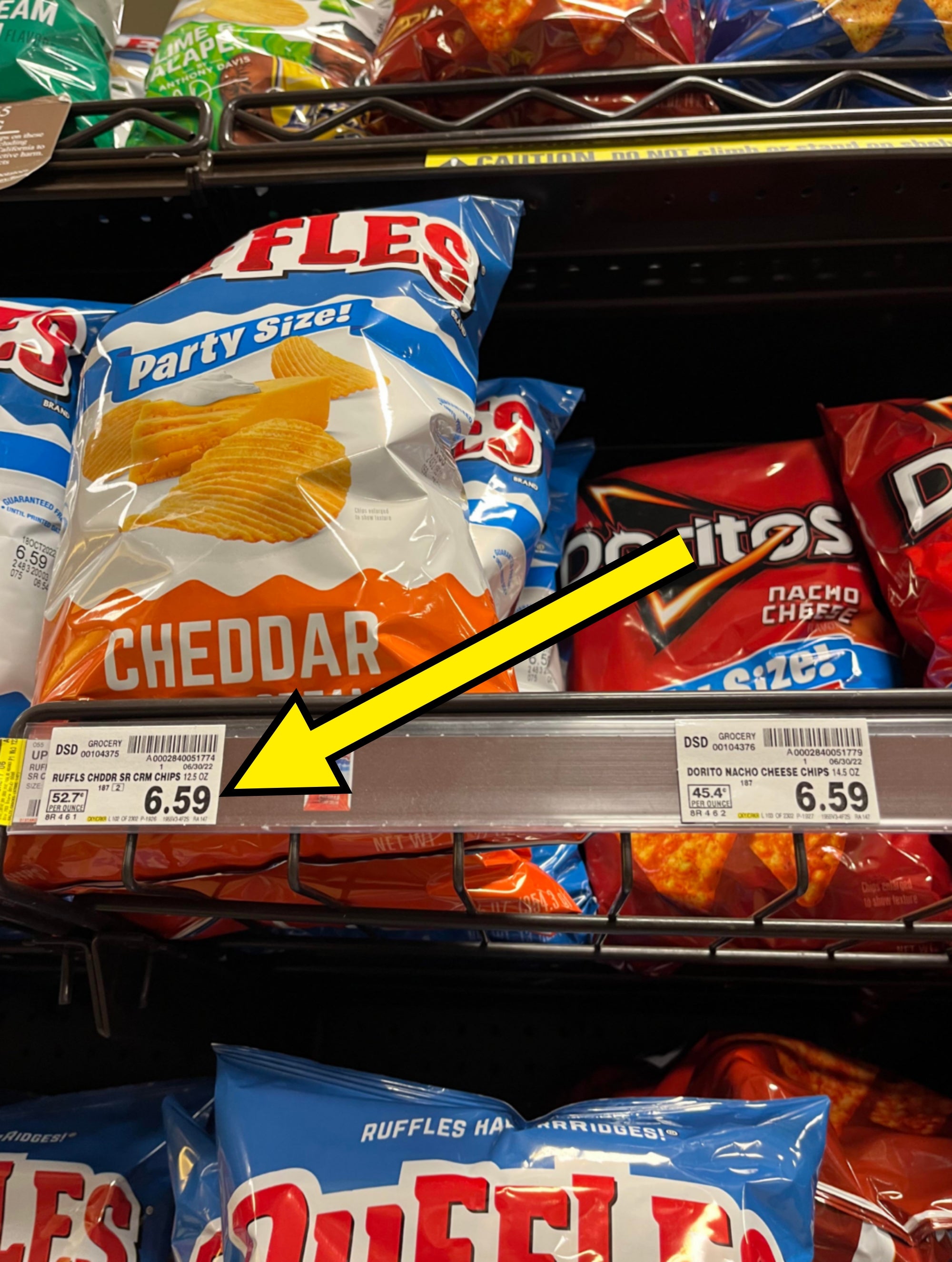 Shelf displaying bags of Ruffles cheddar and Doritos Nacho Cheese chips, priced at $6.59 each