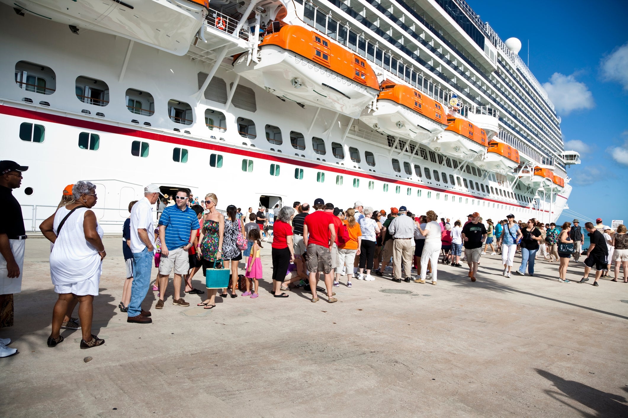 People lined up to board a large cruise ship at the dock, engaging in conversation and carrying luggage