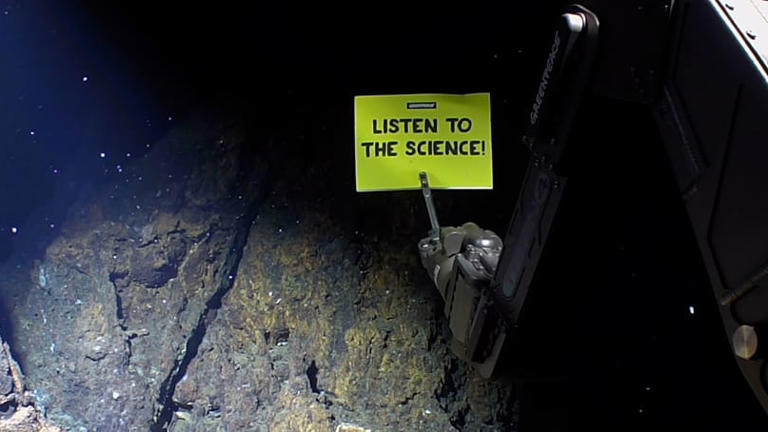 An ROV arm holding a "Listen to the science" poster at the Arctic seabed Greenpeace