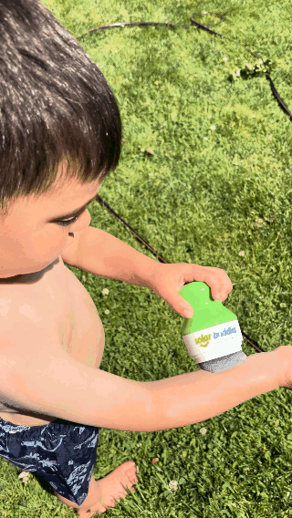 Child using a spray sunscreen bottle on a sunny day outdoors