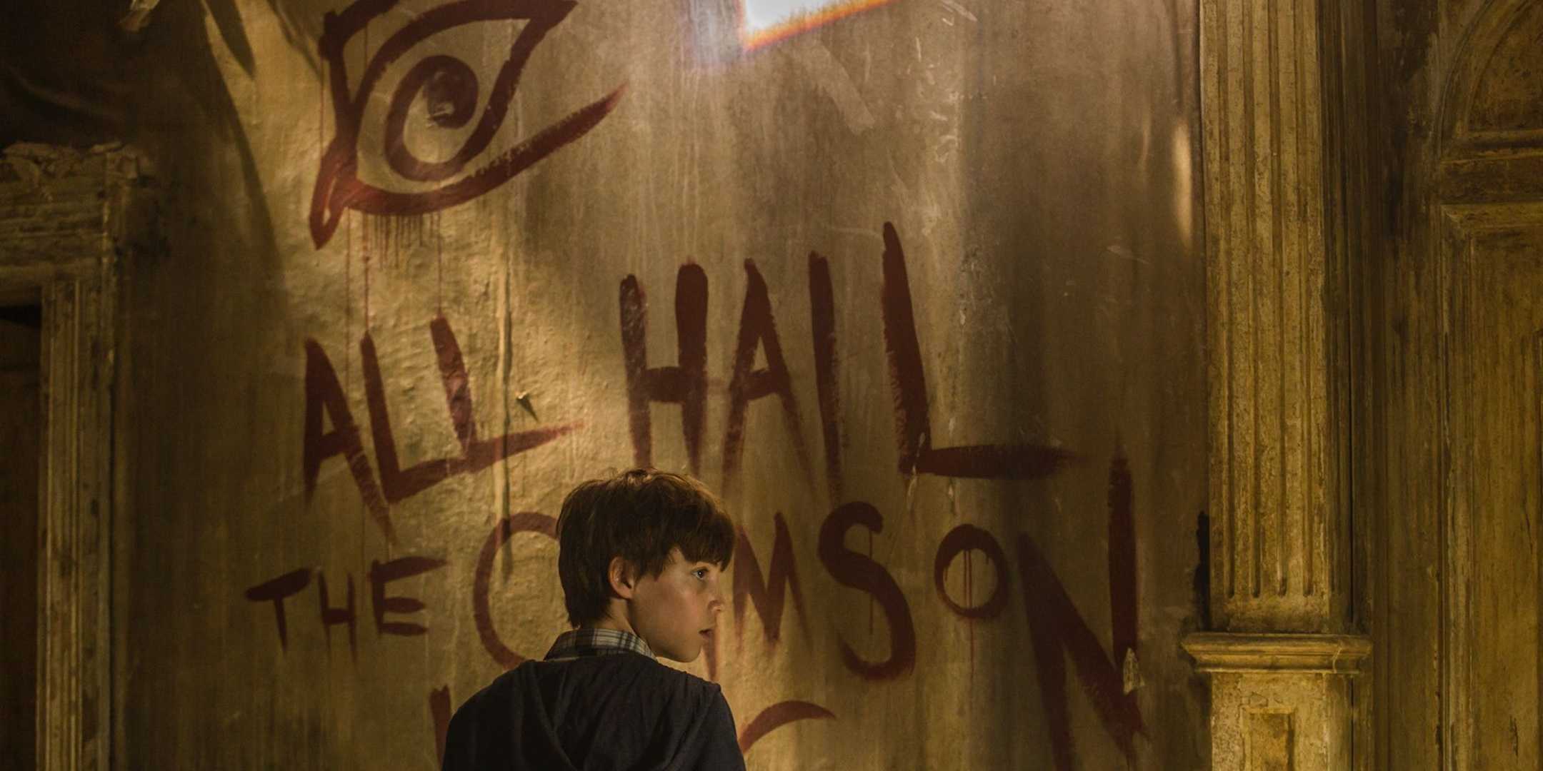 Jake Chambers (Tom Taylor) standing in front of a wall painting saying all Hail the crimson King from the Dark Tower movie