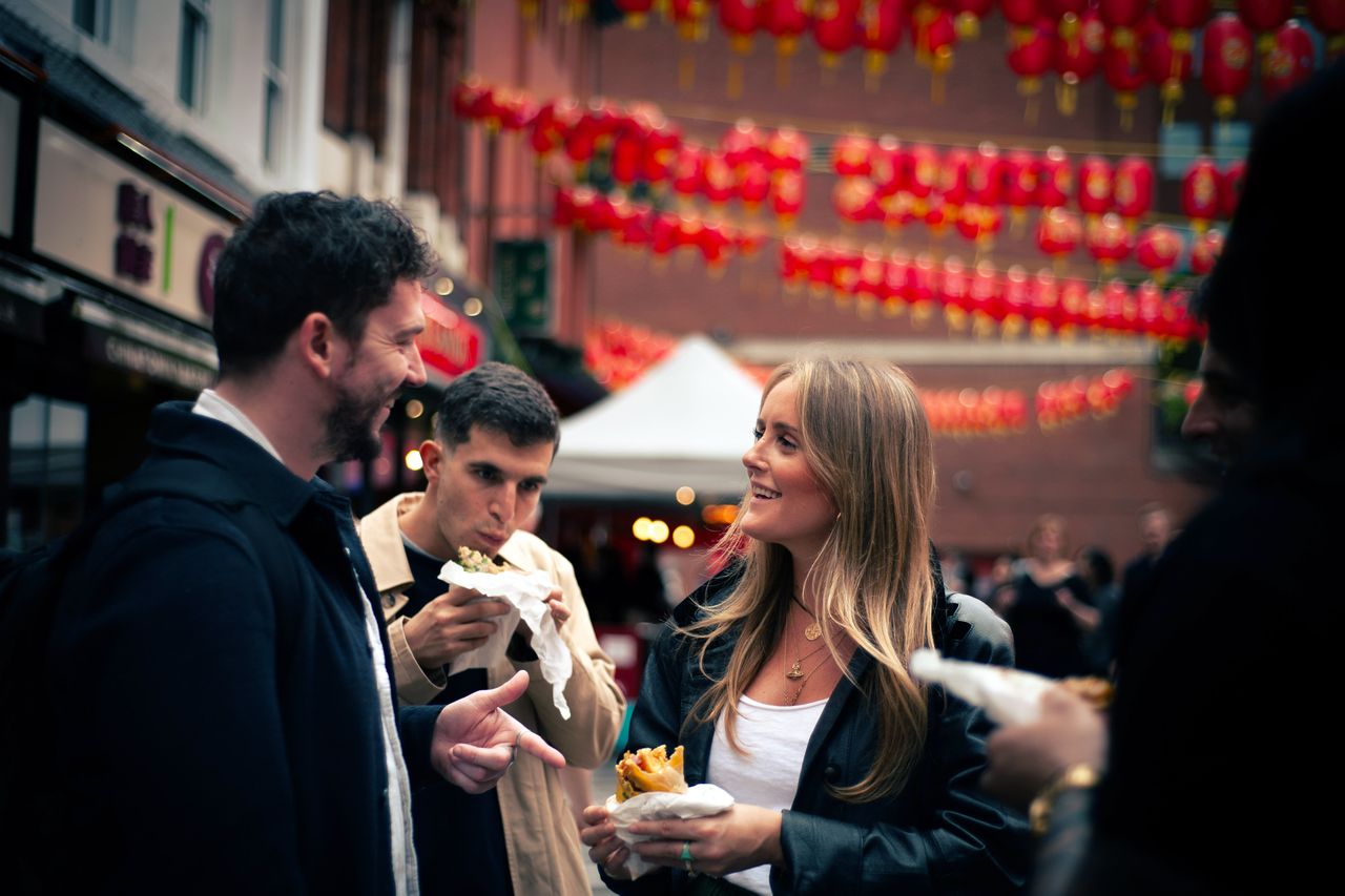 People enjoying street food in an urban outdoor setting with hanging decorations