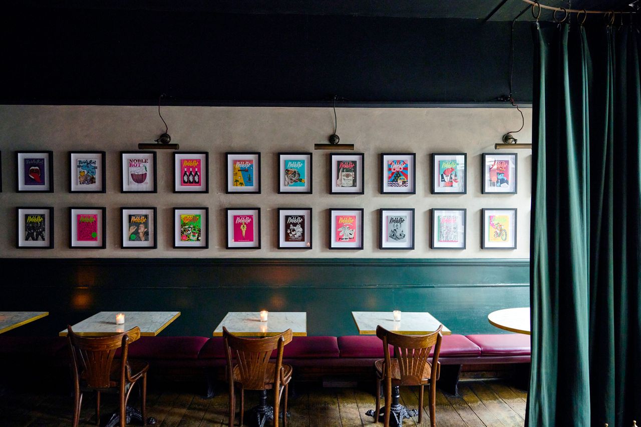 A restaurant interior with framed artwork on the wall and a few tables with chairs