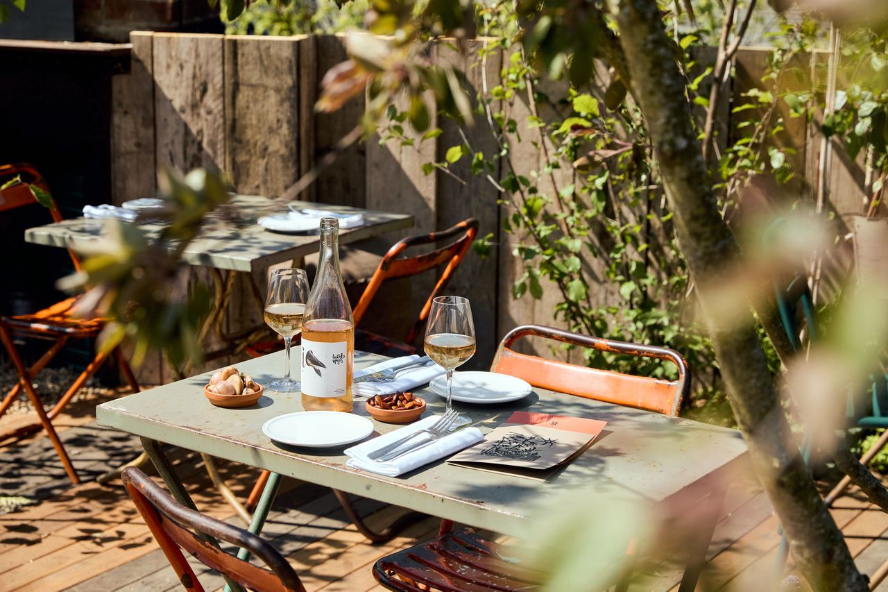 An outdoor table set for dining with wine and snacks surrounded by foliage