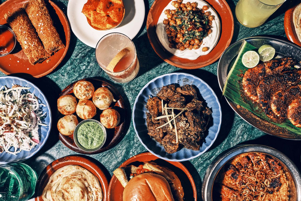 A table filled with various dishes including grilled meat chickpeas rolls curry sauces and bread