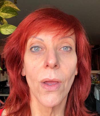 Person with red hair looks into the camera in a casual setting, light makeup visible