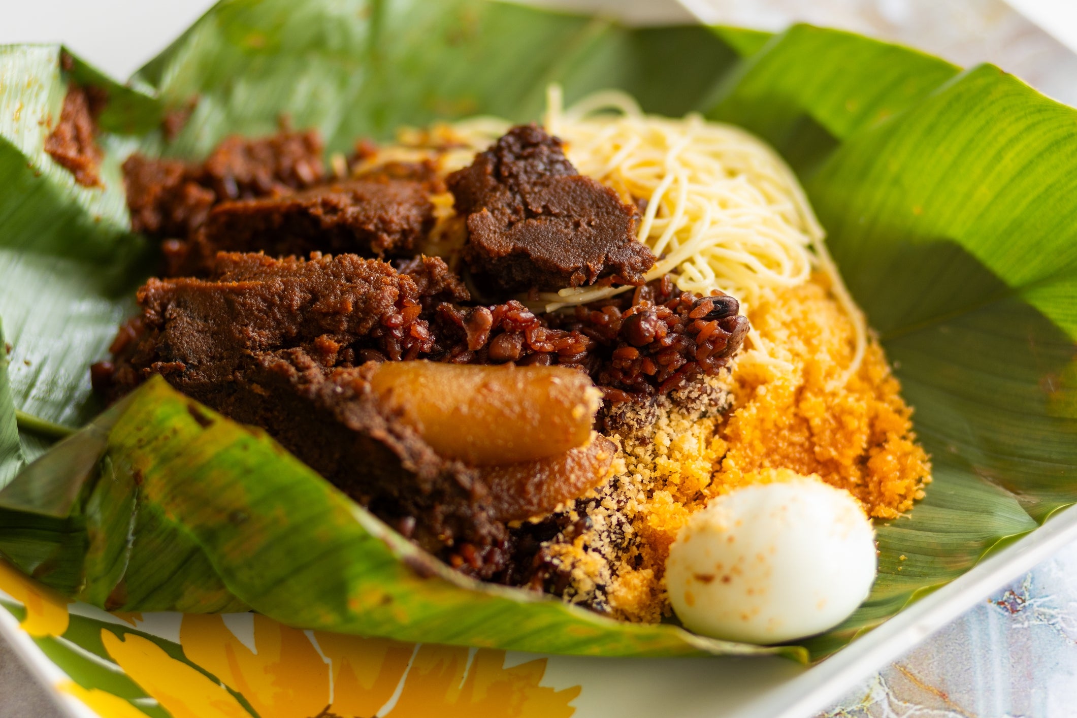 Traditional Nigerian dish served on banana leaves, featuring rice, meat, noodles, egg, and a sprinkle of seasonings