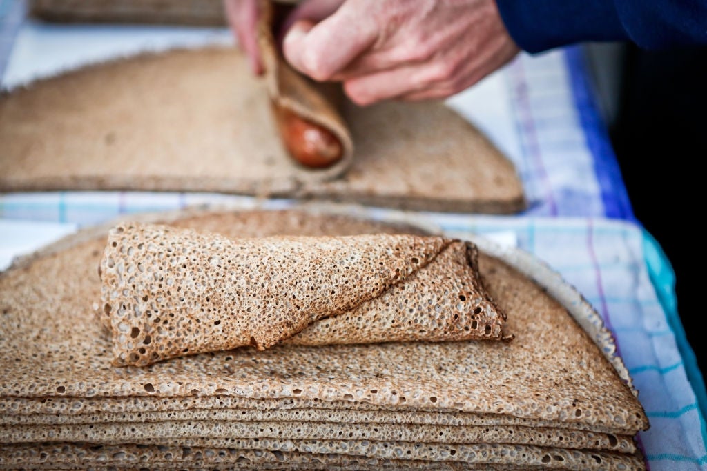 Person rolling a thin, textured crepe on a table covered with stacked crepes