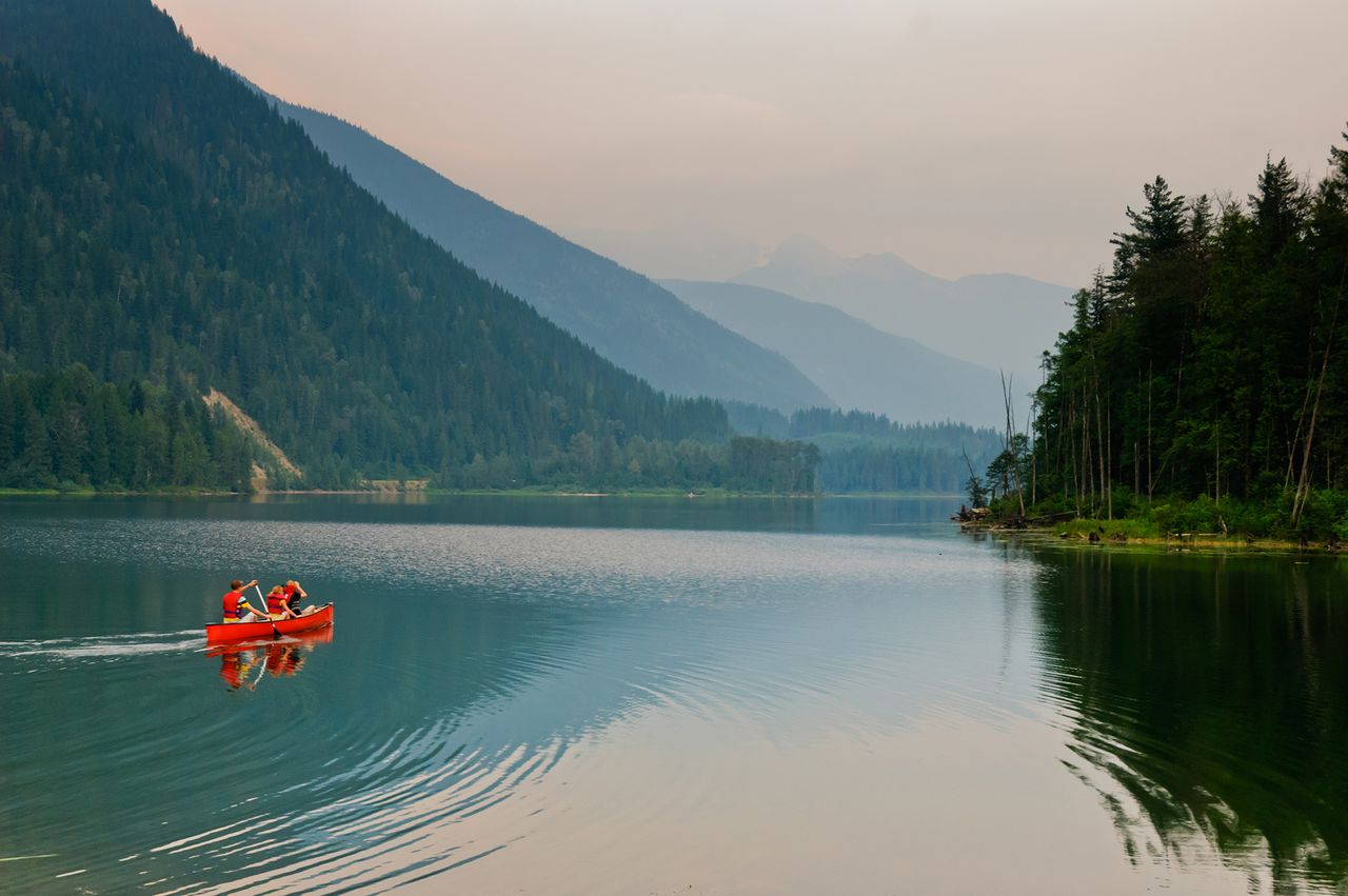 People canoeing on a calm lake surrounded by mountains and trees