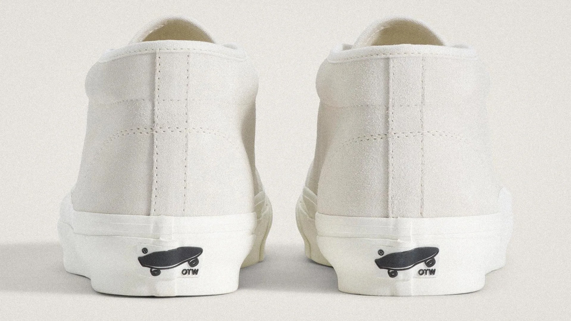 Pair of off-white suede sneakers shown from the back with black skateboard logo on the white rubber sole.