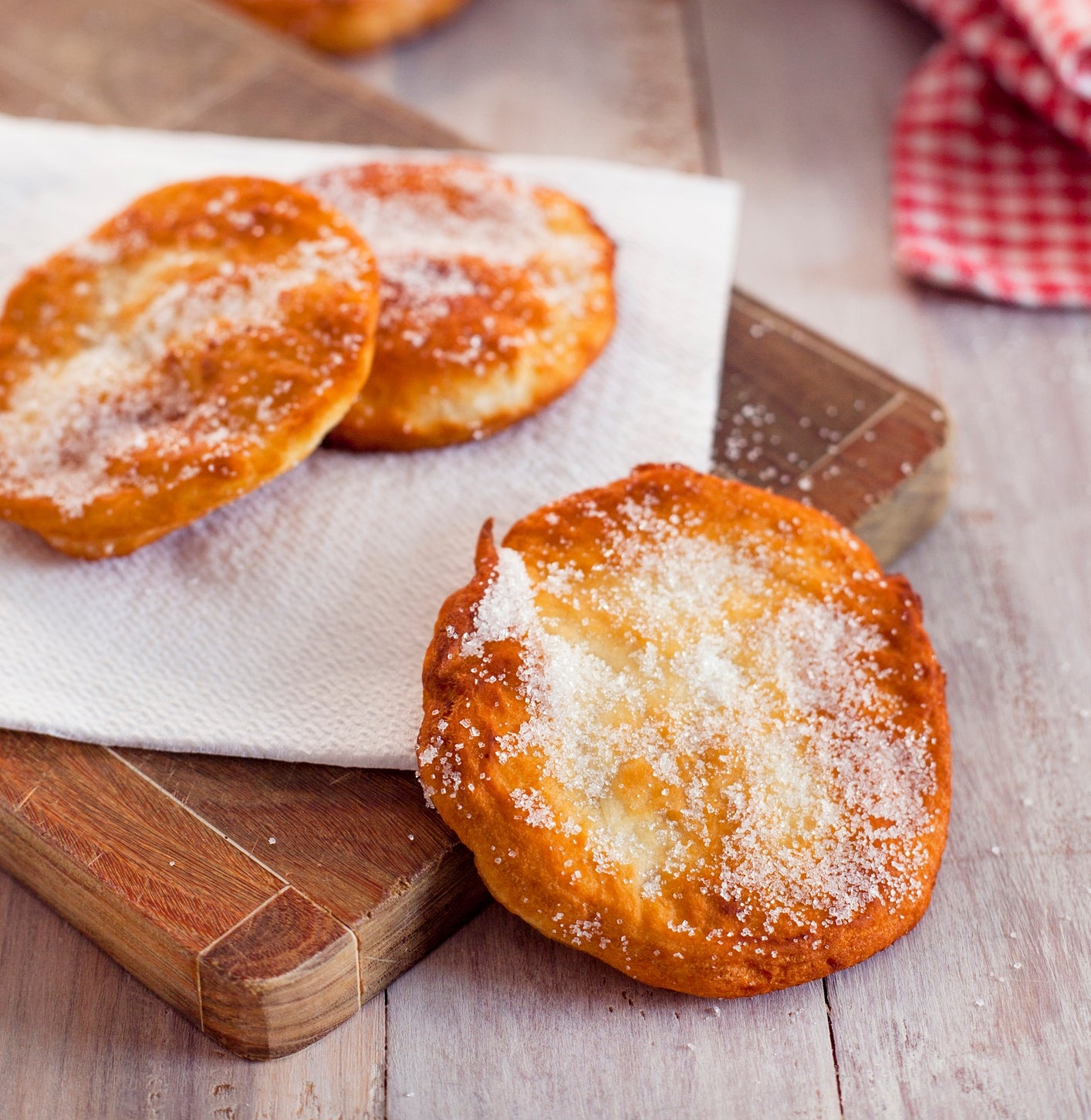 Sugar-dusted fried pastries on a wooden board, with more pastries in a tray in the background