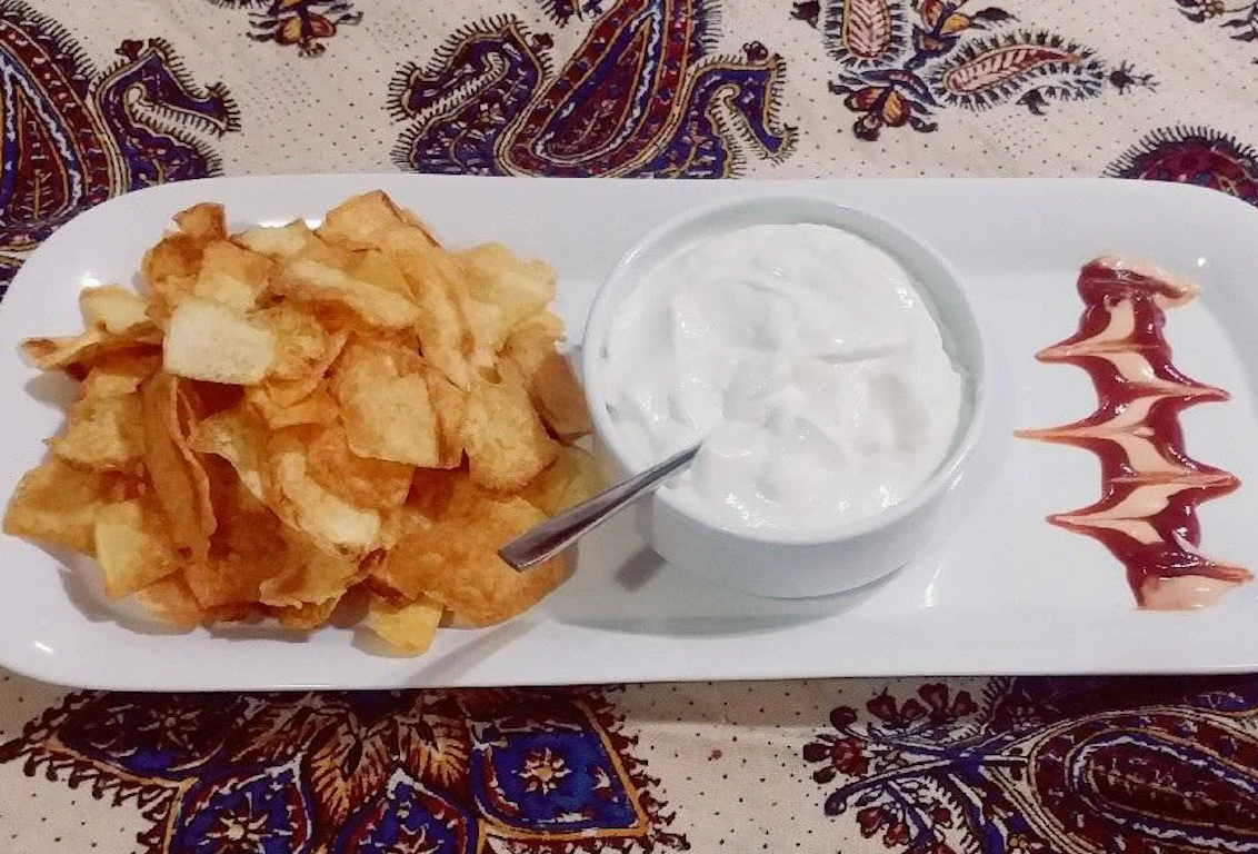 Plate with potato chips, a bowl of dip, and zigzag sauce design on a patterned tablecloth
