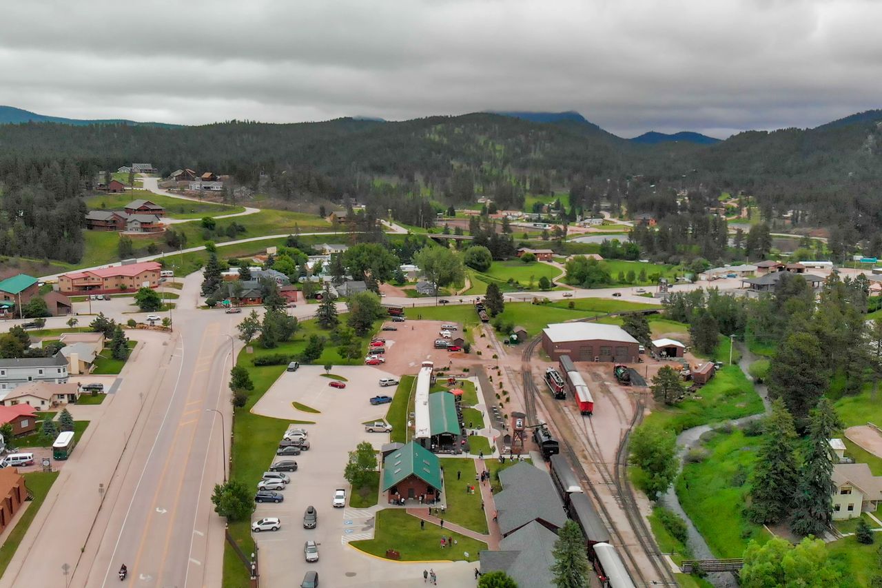 Aerial view of a small town with train tracks and buildings in a valley surrounded by hills and greenery