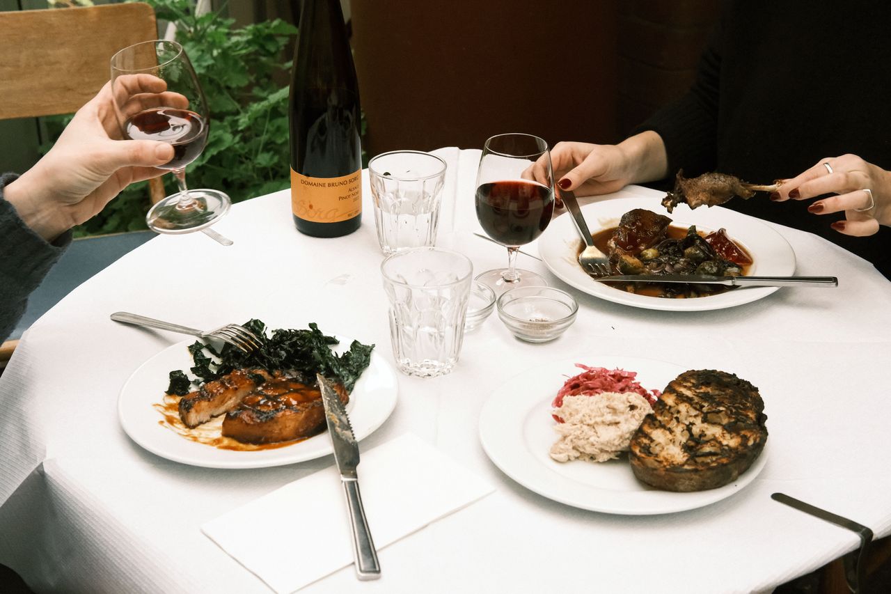 A dining table with plates of food glasses and a bottle of wine showing a meal setting with two individuals