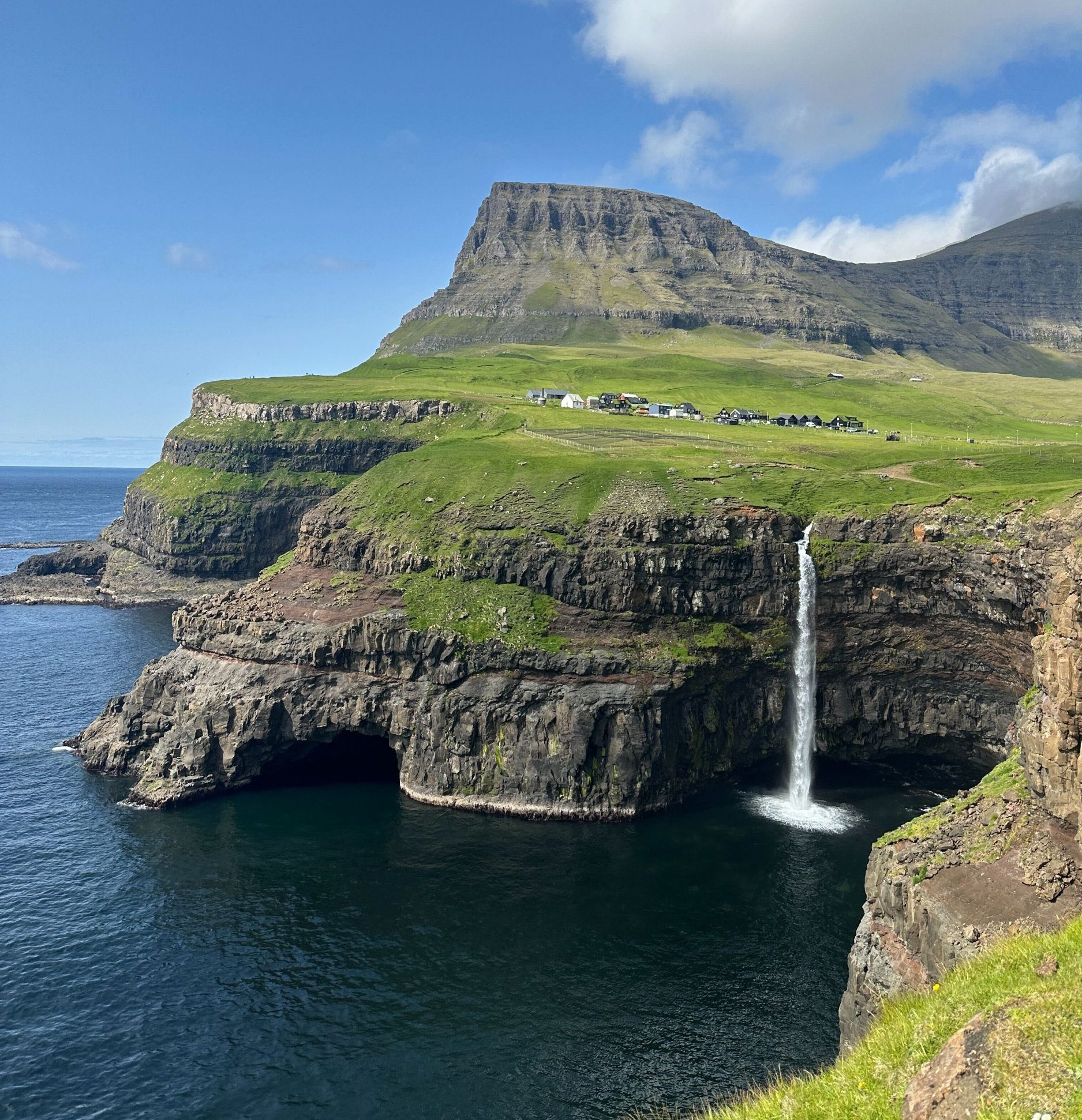A waterfall and hilly outcrop in the Faroe Islands on a bright summer's day