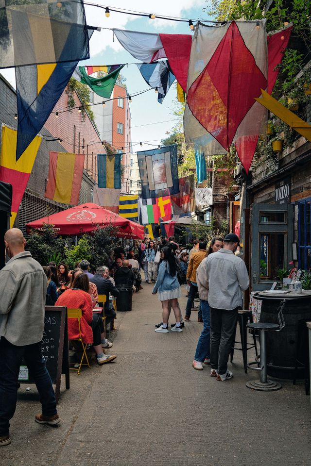 Outdoor market with food vendors and flags hanging overhead people seated and walking through the area