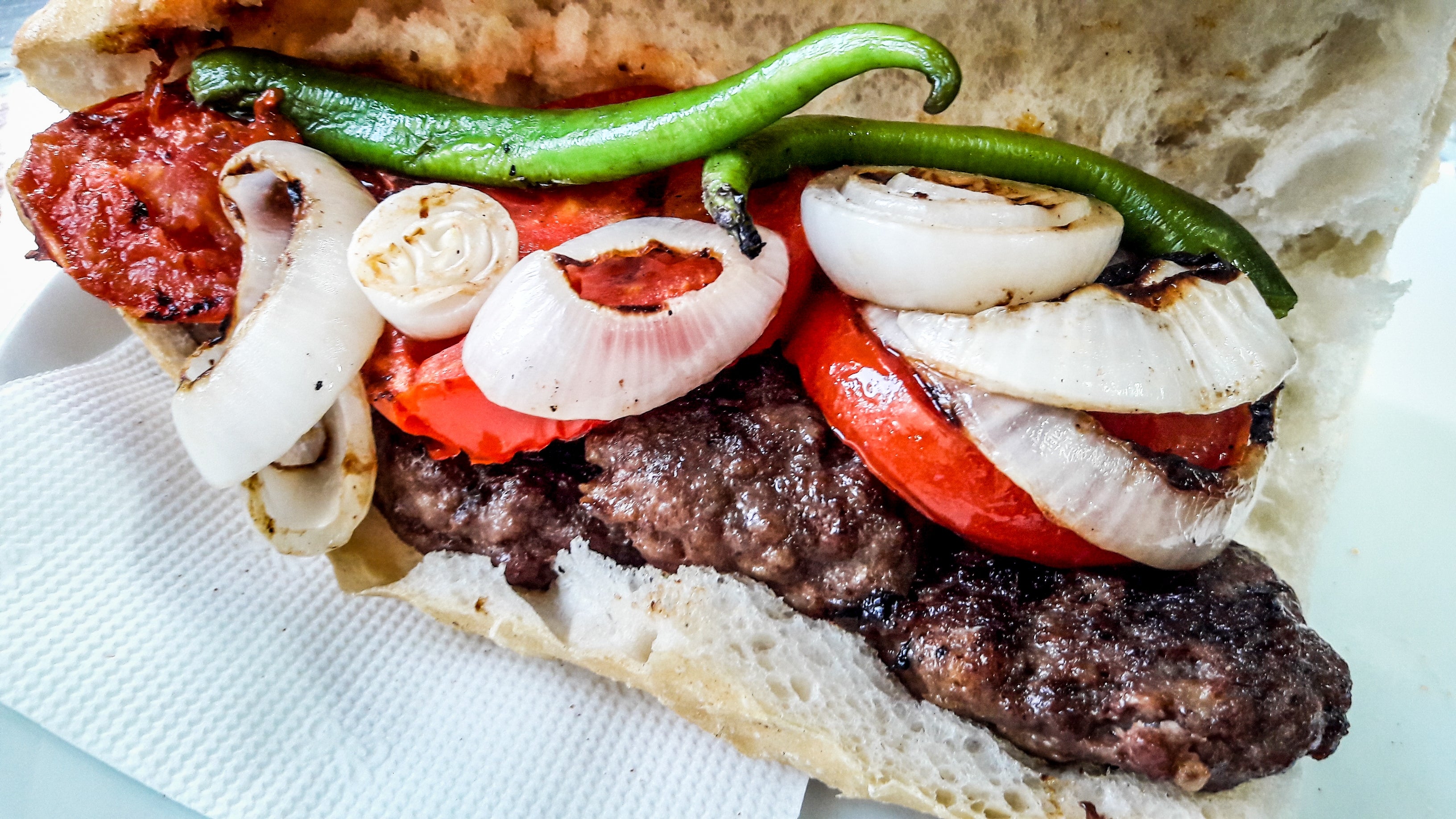 Grilled kebab sandwich with onion, tomato, and chili pepper in bread