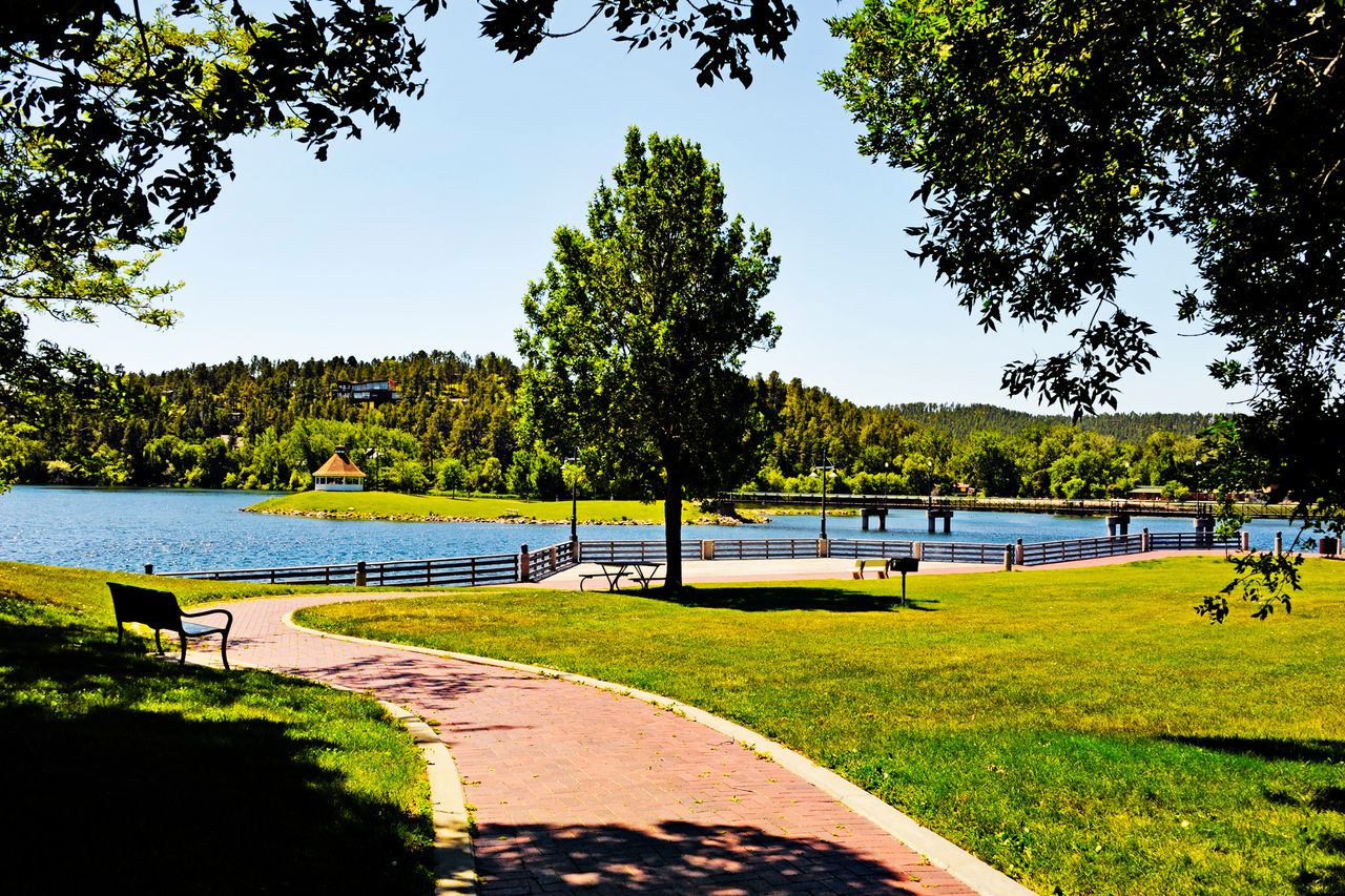 Park landscape with a walking path trees a lake and a bridge visible in the distance
