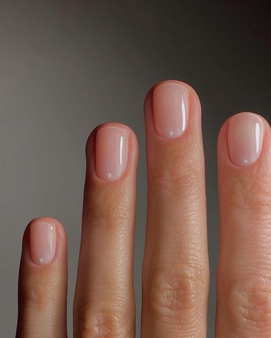 Person shows off their short, clear nails with white dots at the base of each nail