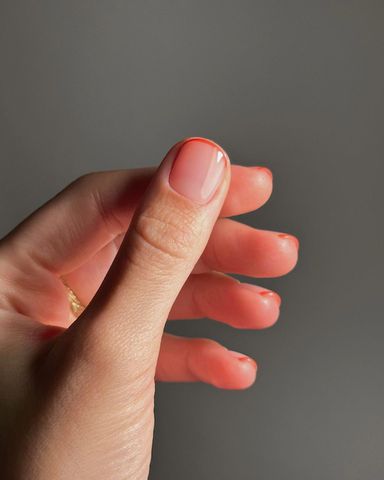Person shows off their clear manicure with thin, orange French tips