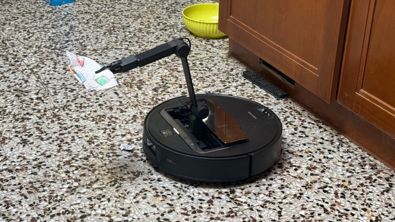 A robot vacuum with a flexible arm picking up a paper towel from the floor