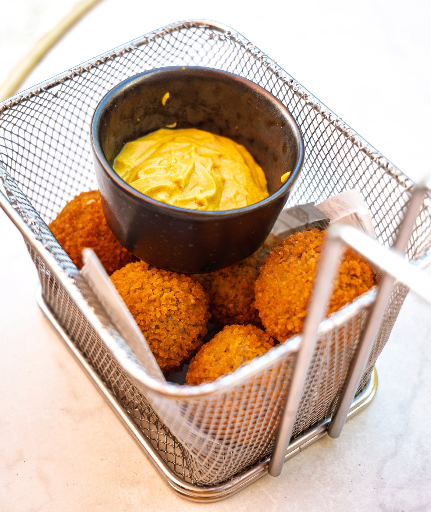 Falafel balls in a wire basket with a small bowl of dipping sauce, placed on a table