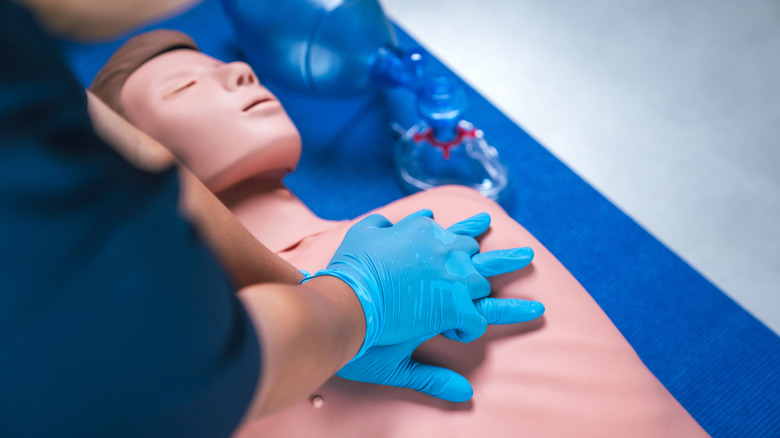 Someone with gloves performing CPR on a test dummy.