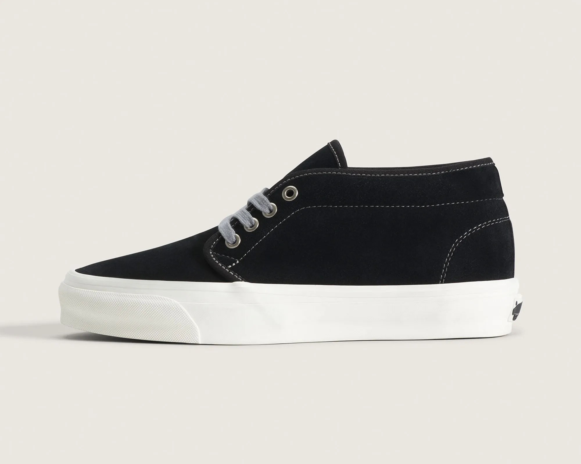 Black suede high-top sneaker with white rubber sole and gray laces on a beige background.