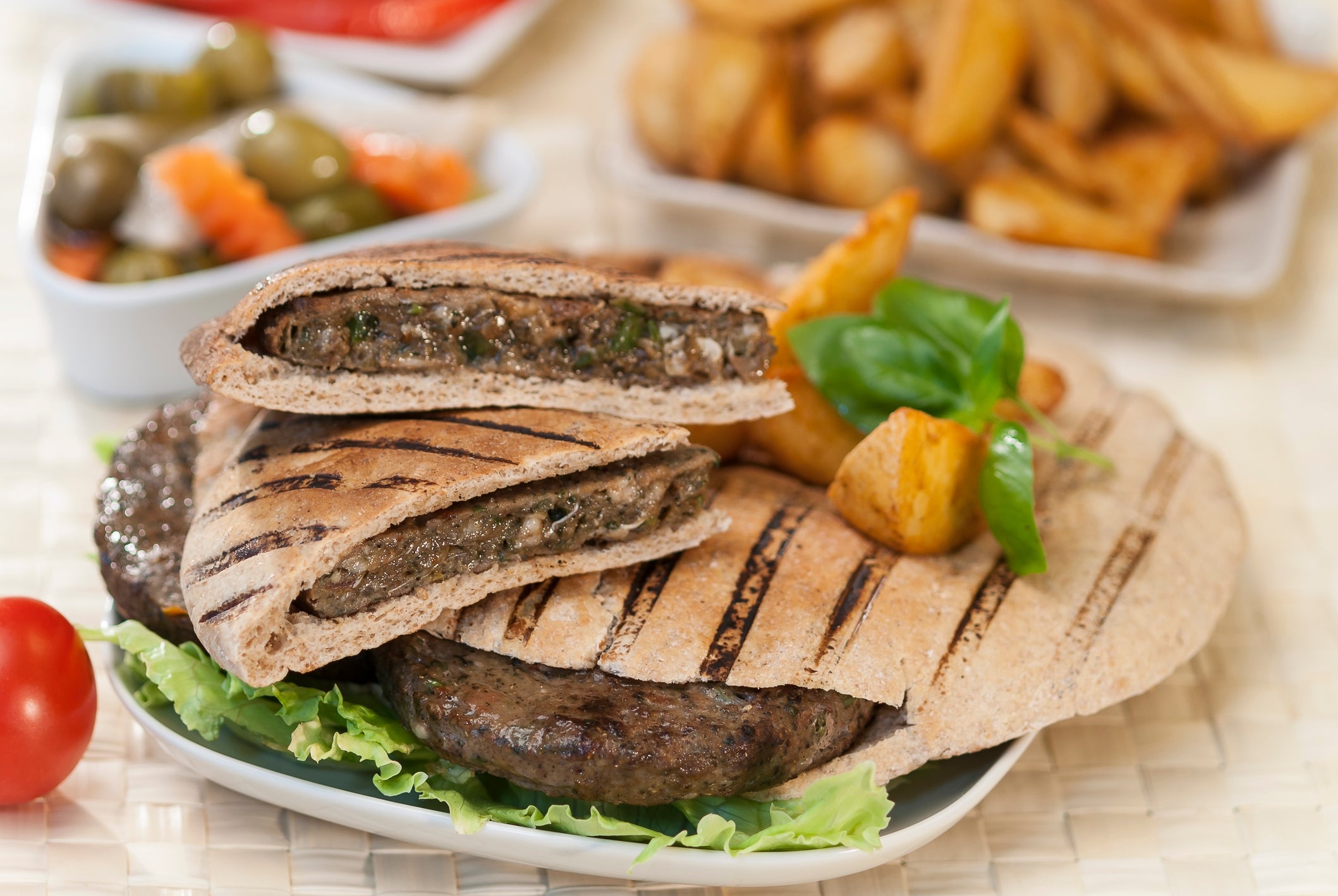 Grilled wrap sandwich featuring spiced meat patties, lettuce, potato wedges, olives, and pickles