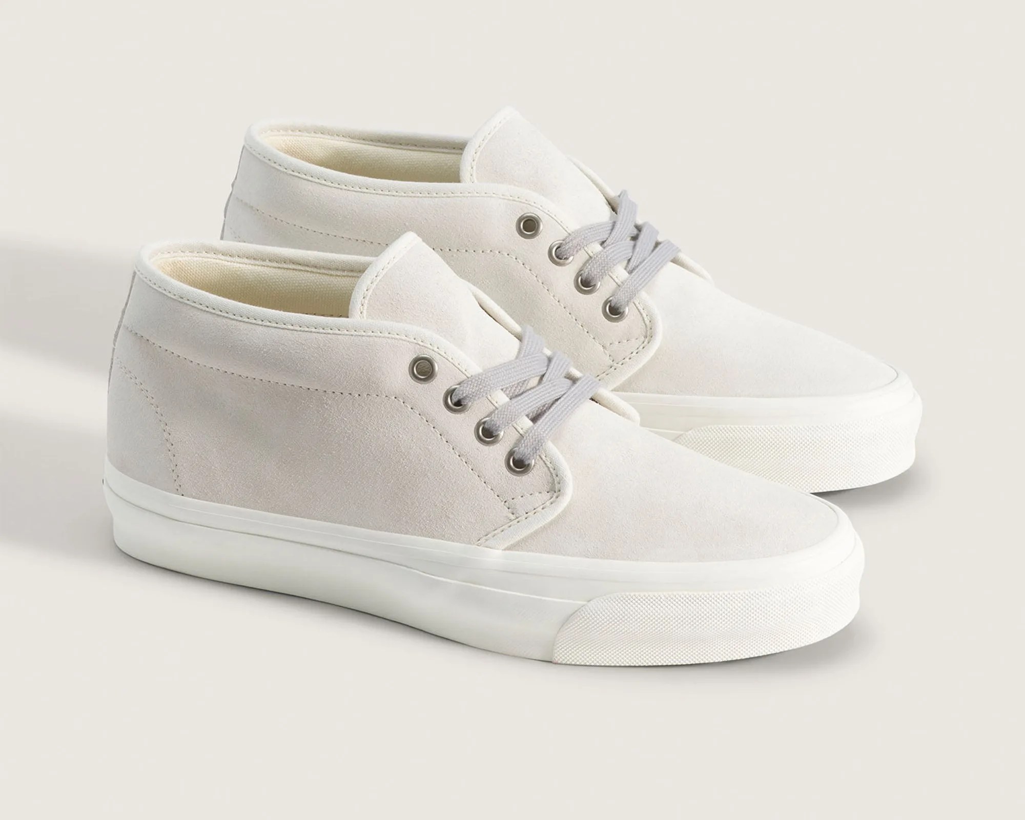 Pair of off-white suede mid-top sneakers with gray laces and white rubber soles.