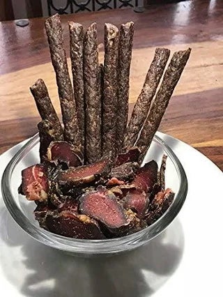 A glass bowl filled with biltong strips and sticks arranged upright on a wooden table