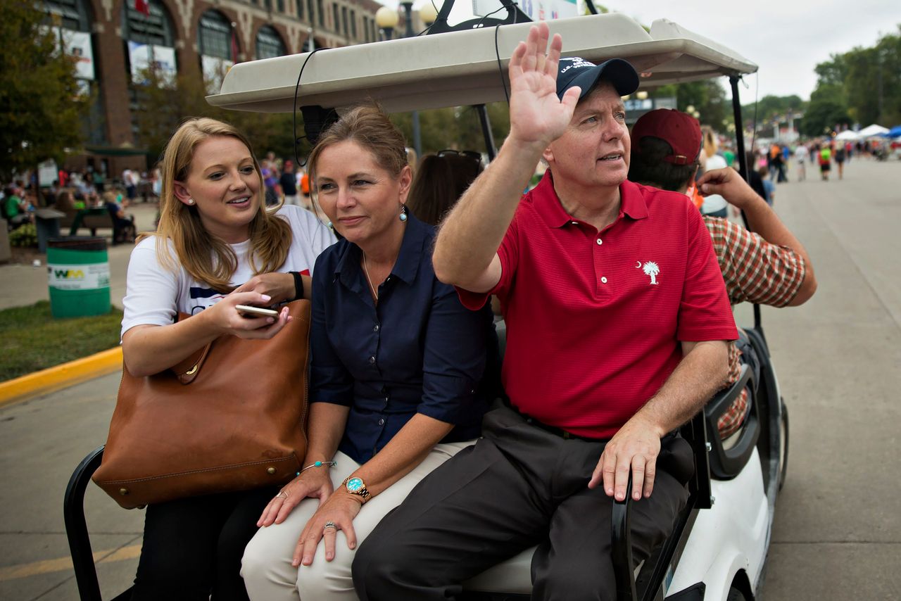 Senator Lindsey Graham, a Republican from South Carolina and 2016 Republican presidential candidate, right, waves to attendees while riding in a golf cart to a television interview with his sister Darline Graham Nordone, center, during the Iowa State Fair in Des Moines, Iowa, U.S., on Monday, Aug. 17, 2015. Graham said he'll use his subcommittee chairmanship to cut off U.S. financing for the International Atomic Energy Agency unless it provides Congress with copies of confidential agreements between the agency and Iran on the country's nuclear program.