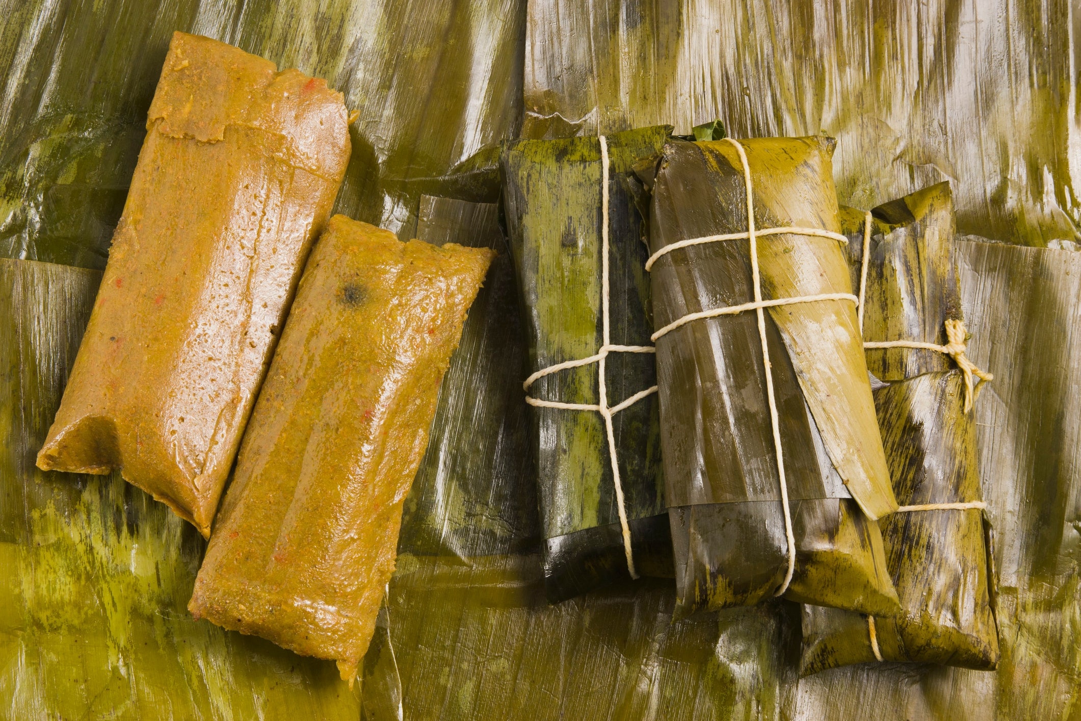 Two types of tamales: uncovered on the left and wrapped in banana leaves with string on the right, displayed on banana leaves