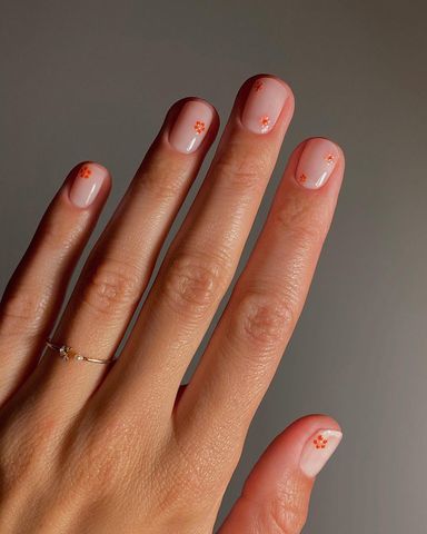 Clear manicure with one to two small, orange flower details on each finger
