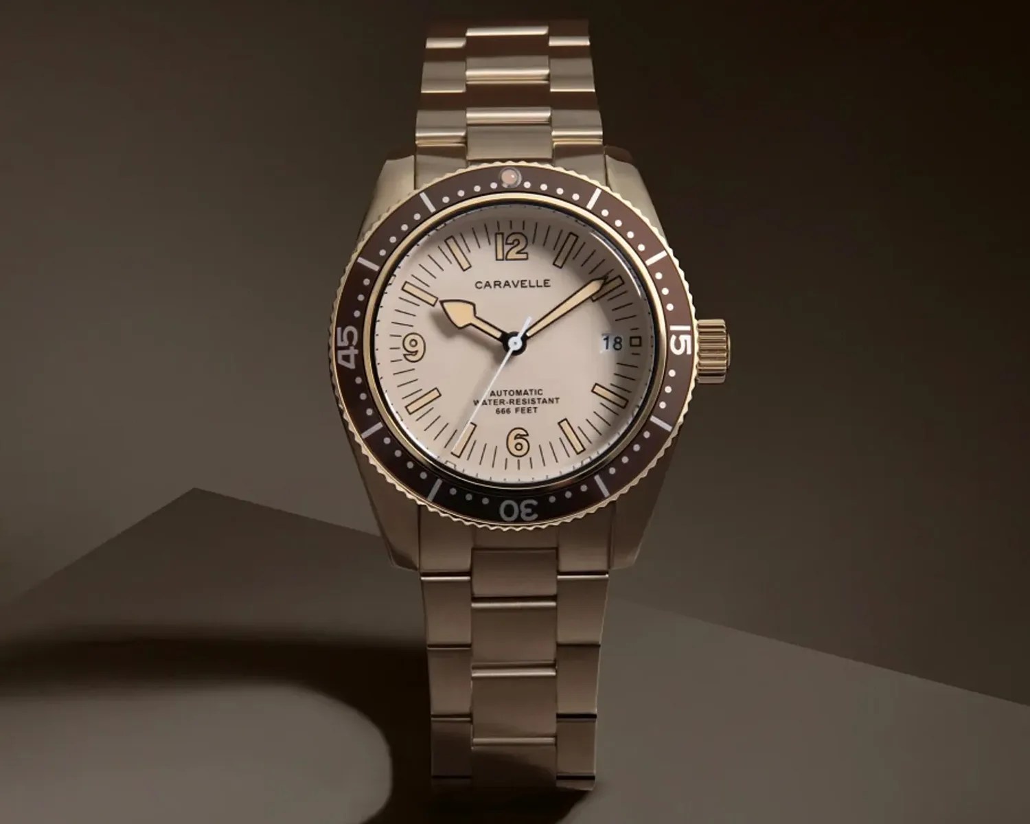 Gold-tone metal wristwatch with beige dial, black bezel, and date window at 3 o'clock.