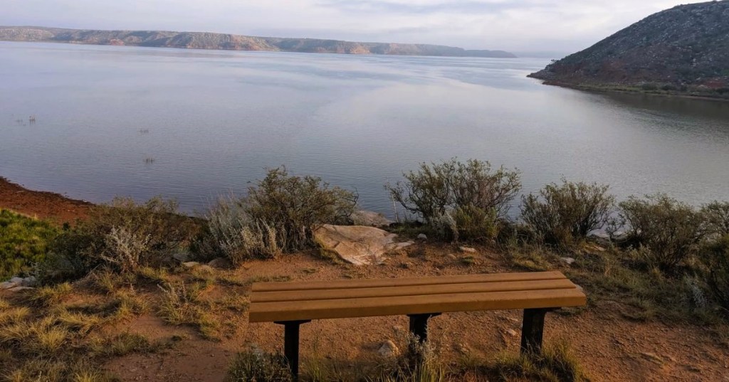 Views from an overlook of Lake Meredith in Texas, with a bench and surrounded by shrubs.