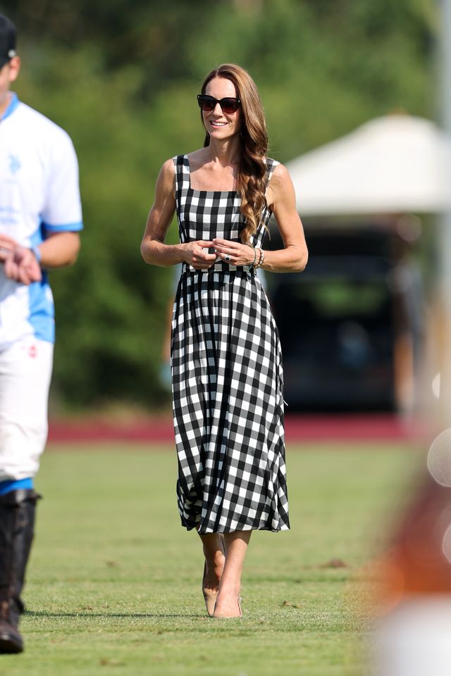 A woman standing outdoors wearing a gingham dress holding an object in her hands