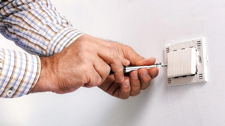 Man using a multitool to adjust a wall outlet