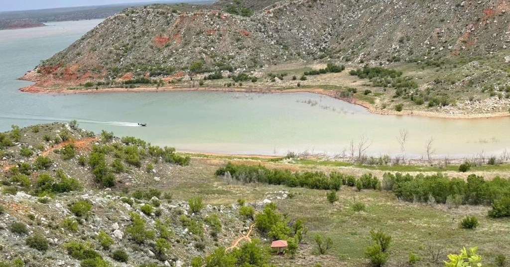 A boat gliding across a channel along Lake Meredith in Texas, featuring calm waters and rugged terrain.