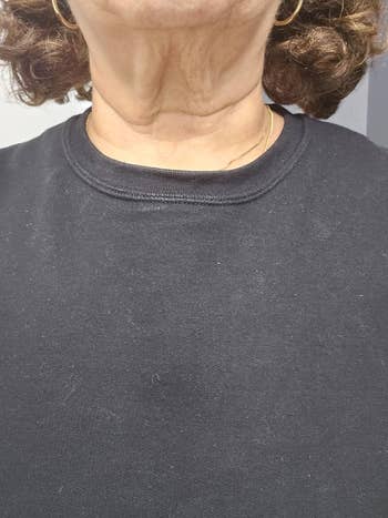 Close-up of a person wearing a plain black sweatshirt with a simple round neckline. Clothing texture is visible