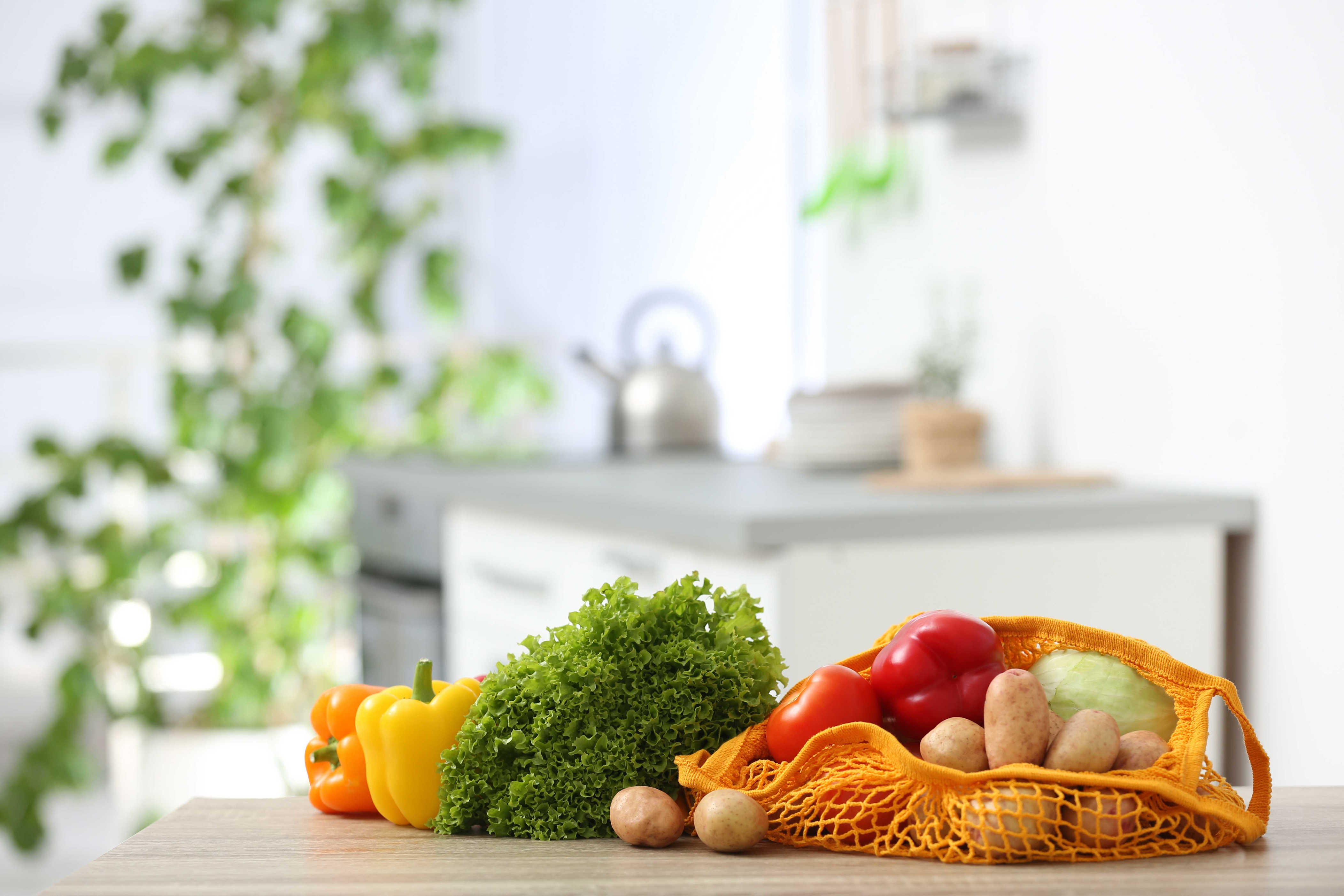 Fresh vegetables in a reusable mesh shopping bag on a kitchen counter.