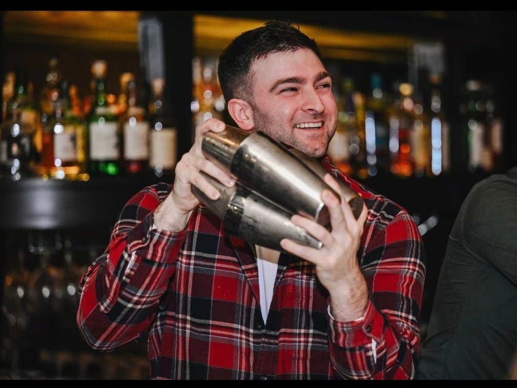 A bartender in a red flannel shirt is shaking a cocktail.