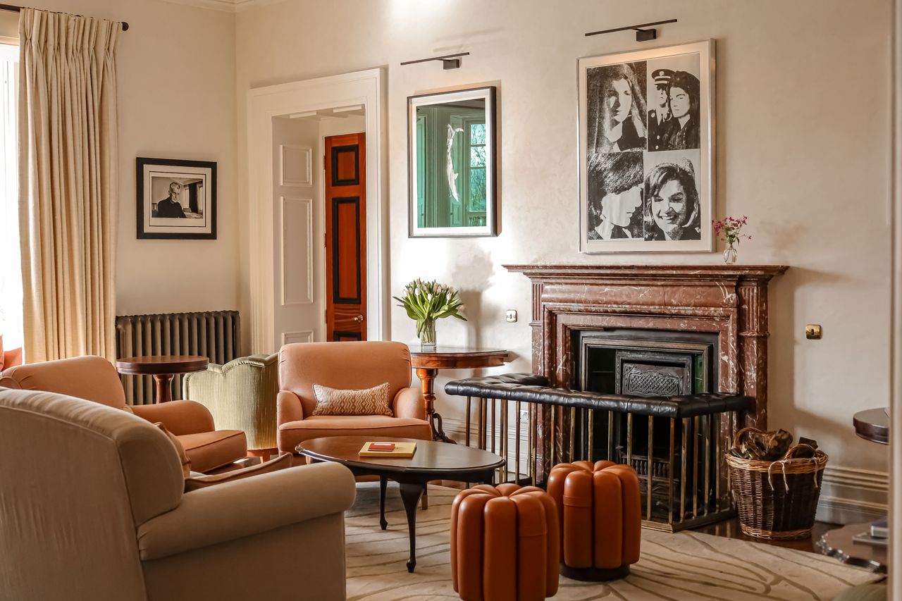 A decorated hotel sitting room with chairs a coffee table a fireplace and framed photographs on the wall
