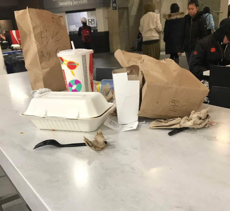 Restaurant table with leftover trash left behind, including a paper bag, cup, and food containers