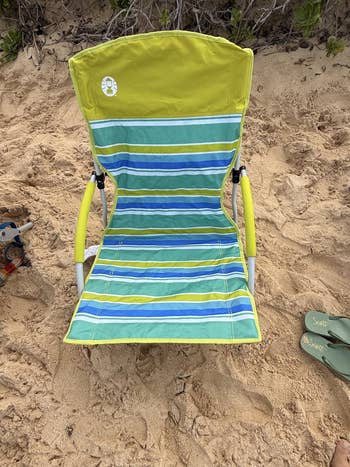 Striped beach chair on sand with nearby flip-flops, suggesting a coastal leisure setting
