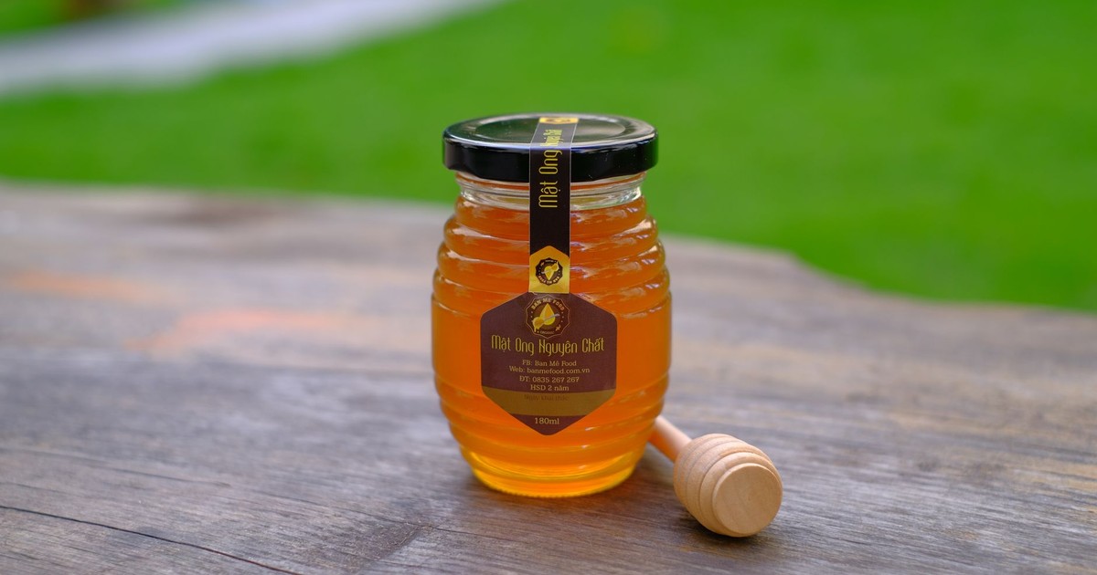 A glass jar of honey with a dipper on a rustic wooden table outdoors.