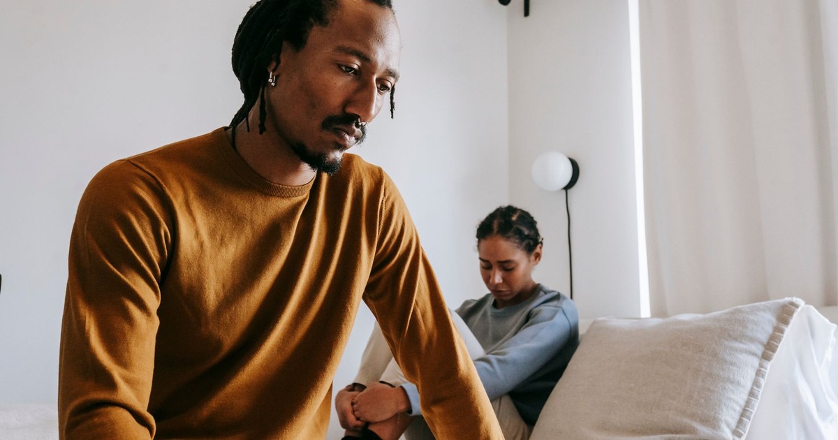 Young sad African American male near frustrated female partner sitting on bed during conflict at home