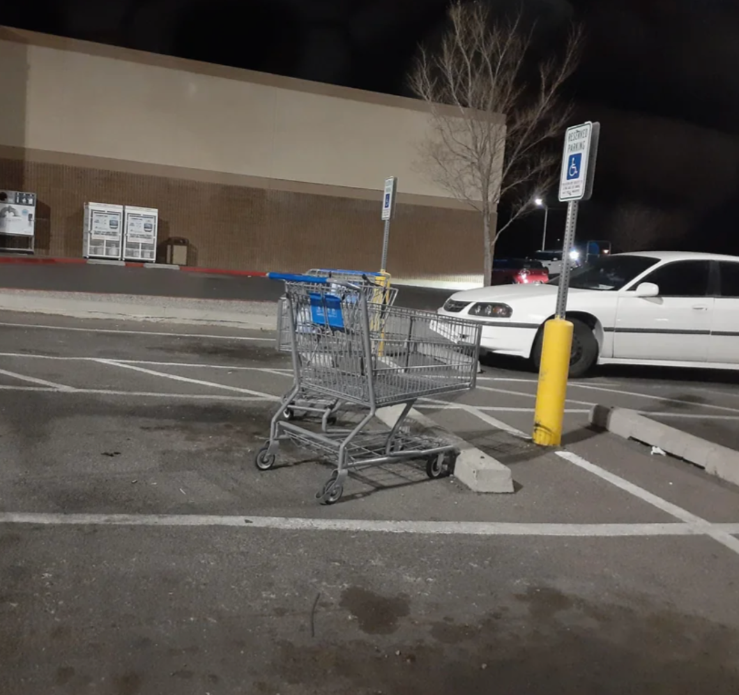 Shopping cart left in handicap parking space at night, empty lot visible in background